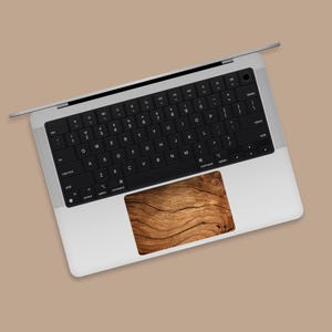 May include: A silver laptop computer with a black keyboard and a wood-grain textured trackpad.