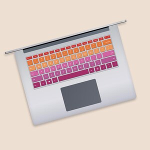 May include: A silver laptop with a colorful keyboard sticker. The sticker features a gradient of orange, pink, and red colors. The keys are labeled with the standard English alphabet.