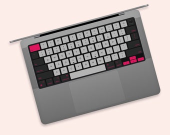 Może przedstawiać: Szary laptop z czarną klawiaturą i gładzikiem. Klawiatura ma białe klawisze z czarnymi napisami i różowymi akcentami. Klawisze są oznaczone literami, cyframi i symbolami.