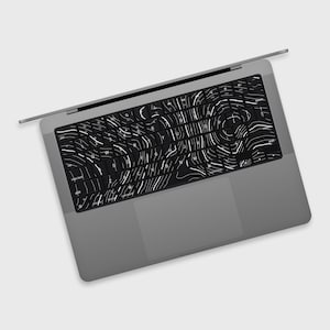 May include: A grey laptop with a black keyboard cover featuring a white topographic design. The laptop is open, showing the keyboard and trackpad. The keyboard cover has a unique, artistic pattern.
