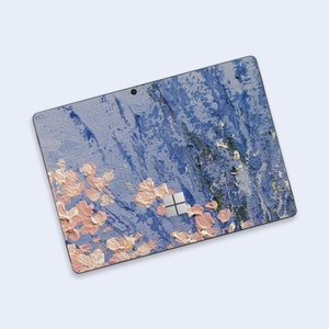 Könnte beinhalten: Blaue und rosafarbene abstrakte Kunst-Laptop-Haut mit einem strukturierten Farbeffekt. Die Haut hat ein kleines, quadratisches, silbernes Microsoft-Logo in der Mitte.