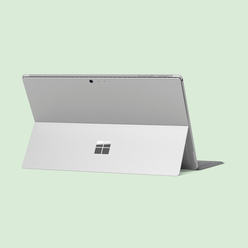 May include: A silver laptop computer with a black keyboard. The laptop is closed and the Microsoft logo is visible on the back.