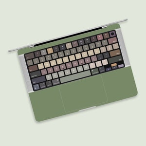 Könnte beinhalten: Ein grüner Laptop mit einer Tastatur in gedeckten Farben und einem Trackpad. Die Tasten haben verschiedene Brauntöne, Grautöne und Beige.