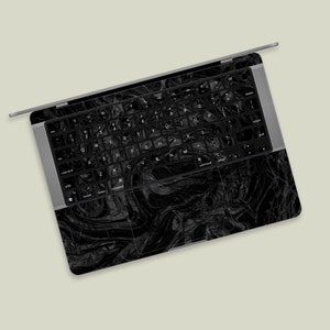 May include: A black laptop computer with a black and white marbled design on the lid and keyboard. The laptop is open and the keyboard is visible. The keys are labelled with the standard English alphabet.