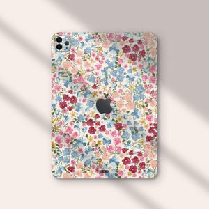 Puede incluir: Una funda de tel&eacute;fono floral con fondo blanco y una variedad de flores rosas, azules y rojas. La funda tiene un recorte para el logotipo de Apple.