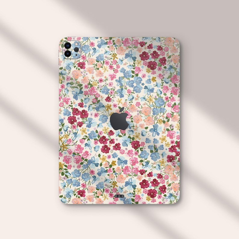 Puede incluir: Una funda de tel&eacute;fono floral con fondo blanco y una variedad de flores rosas, azules y rojas. La funda tiene un recorte para el logotipo de Apple.