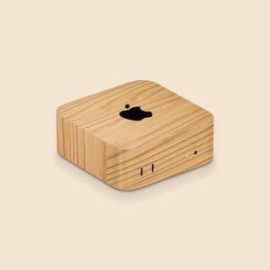 May include: A light-colored wooden electronic device with a black Apple logo on top. The device has a rectangular shape with rounded edges and two small horizontal lines on the front.