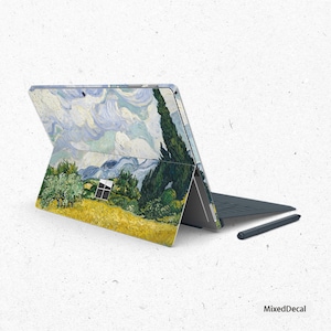 May include: A laptop computer with a blue and green landscape design on the lid. The laptop is closed and the screen is facing away from the viewer. A stylus pen is lying on the table next to the laptop.