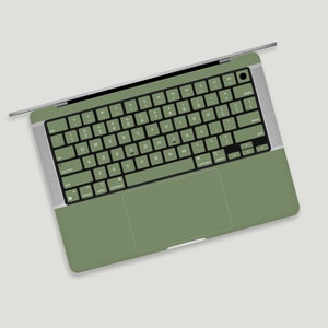 Può includere: Un computer portatile verde con una tastiera e un trackpad argentati. I tasti sono etichettati con lettere e numeri.