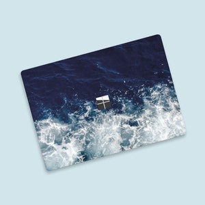 May include: A laptop skin featuring a blue and white ocean wave design. The skin has a cutout for the Microsoft logo.