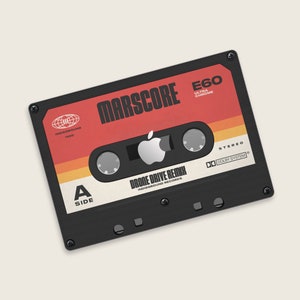 Könnte beinhalten: Ein schwarzes Kassettenband mit einem roten und orangefarbenen Etikett. Das Etikett trägt die Aufschrift "MARSCORE E60 ULTRA CHROME" und "DRONE DRIVE REMIX INDIEGROUND RECORDS". Das Band ist mit "A SIDE" beschriftet und trägt ein Dolby System Logo.