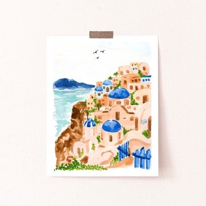 Puede incluir: Una pintura de acuarela de un pueblo blanco y azul en un acantilado con vistas al mar. Los edificios tienen techos abovedados azules y est&aacute;n rodeados de plantas verdes. Hay p&aacute;jaros volando en el cielo.