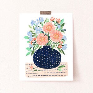 Puede incluir: Un jarr&oacute;n azul con lunares blancos lleno de flores rosas y naranjas y flores azules. El jarr&oacute;n est&aacute; sobre una superficie de rayas rosas y blancas.