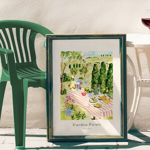 May include: A watercolor painting of a garden picnic scene. The painting features a pink and white striped tablecloth with a variety of food and drinks, including fruit, a watermelon, and a teapot. There are also flowers and birds in the painting. The text "Garden Picnic" is written at the bottom of the painting.
