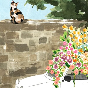 K&ouml;nnte beinhalten: Ein wei&szlig;es Auto mit einem gro&szlig;en Strau&szlig; aus rosa, orangefarbenen und gelben Blumen darauf. Eine dreifarbige Katze sitzt auf einer Backsteinmauer hinter dem Auto.