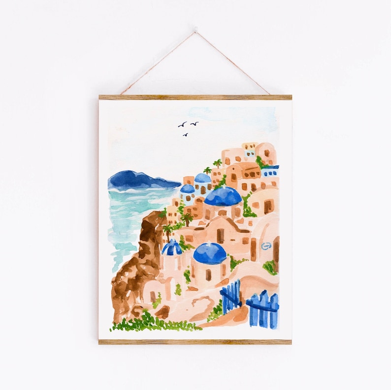 Puede incluir: Pintura acuarela de un pueblo griego blanco y azul en un acantilado con vistas al mar. Los edificios tienen techos abovedados azules y est&aacute;n pintados en tonos de rosa y blanco. El mar es de color azul claro y hay algunas aves volando en el cielo.