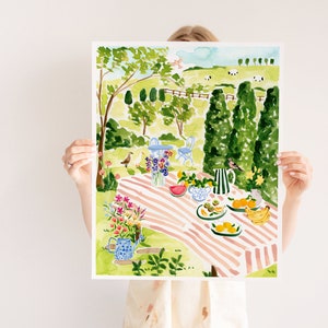 May include: A watercolor painting of a picnic scene in a garden. The painting features a pink and white striped tablecloth, a watermelon, fruit, and flowers. There are trees and a fence in the background.