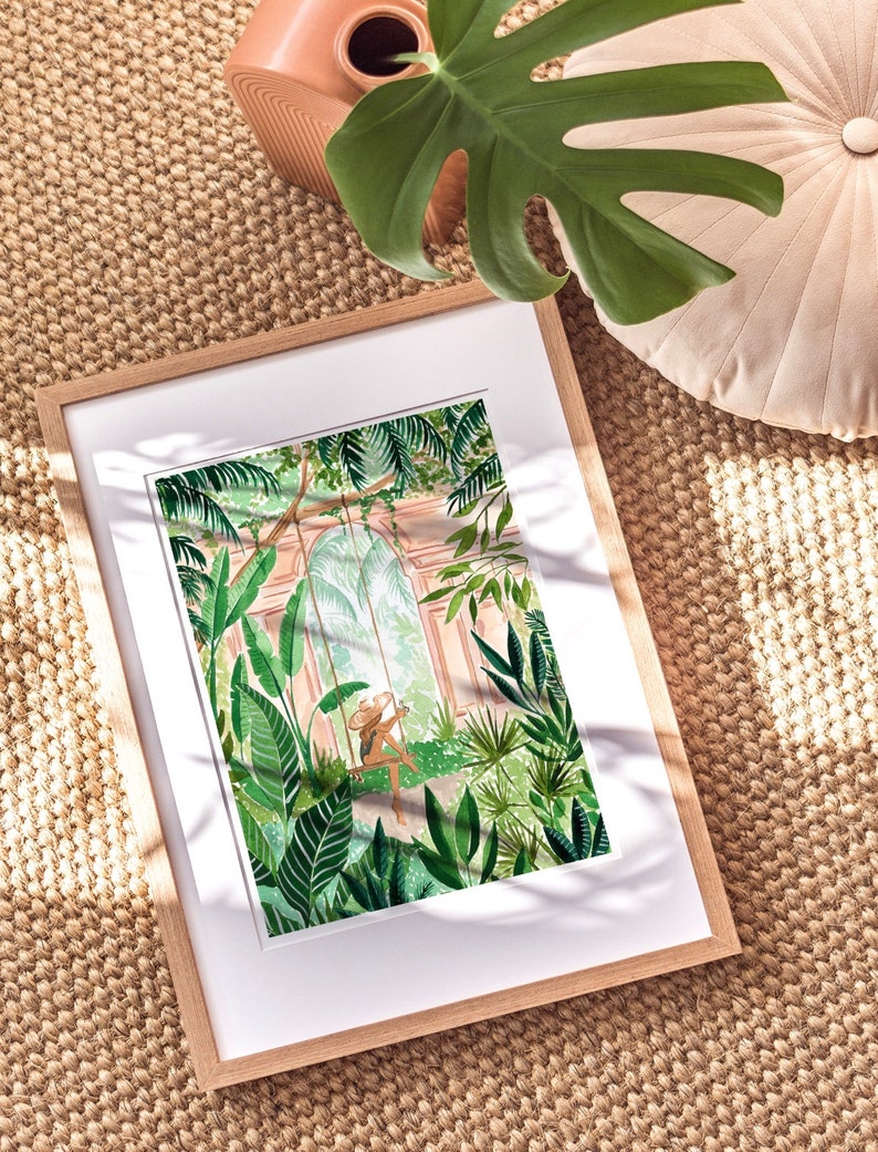 May include: A framed illustration of a woman sitting on a swing in a lush, green jungle. The woman is wearing a straw hat and a white dress. The jungle is filled with large, leafy plants and trees. The illustration is done in a watercolor style.