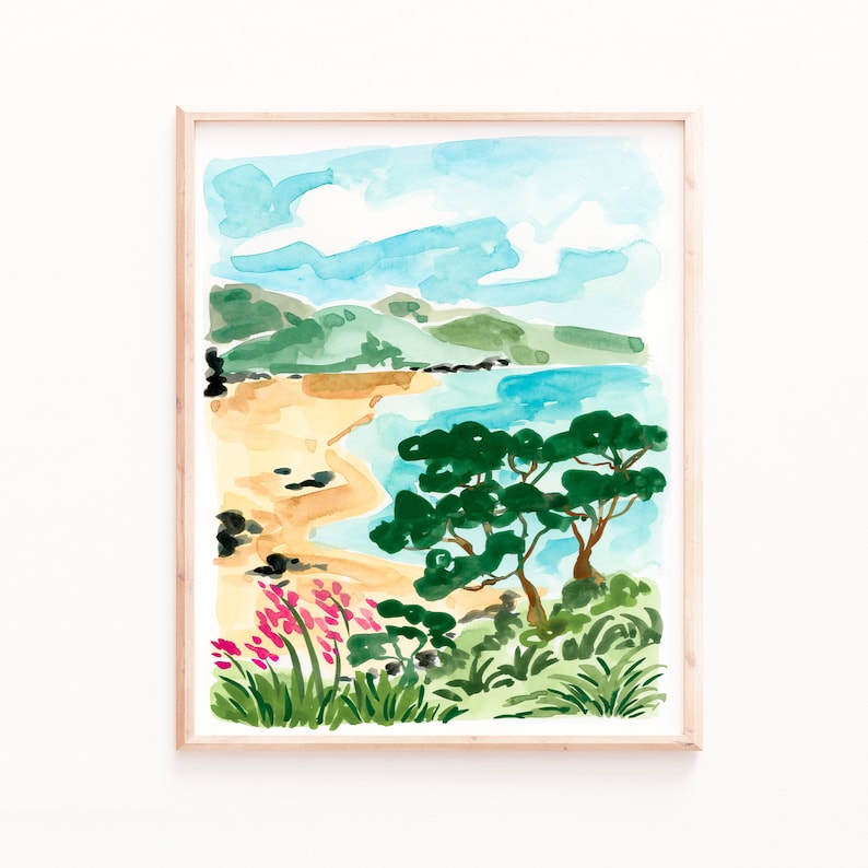 May include: Watercolor painting of a beach scene with a sandy shore, blue water, green trees, and pink flowers. The painting is framed in a light wood frame.