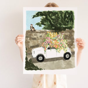 K&ouml;nnte beinhalten: Ein wei&szlig;es Auto mit einem gro&szlig;en Strau&szlig; bunter Blumen auf dem Dach. Das Auto steht vor einer Steinmauer, auf der eine Katze sitzt.