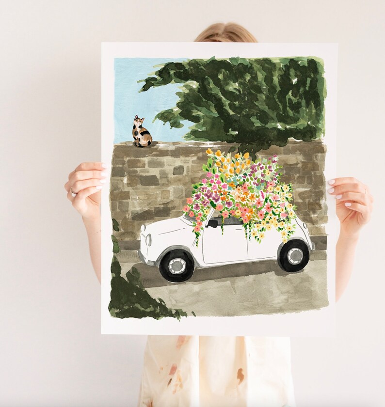 K&ouml;nnte beinhalten: Ein wei&szlig;es Auto mit einem gro&szlig;en Strau&szlig; bunter Blumen auf dem Dach. Das Auto steht vor einer Steinmauer, auf der eine Katze sitzt.