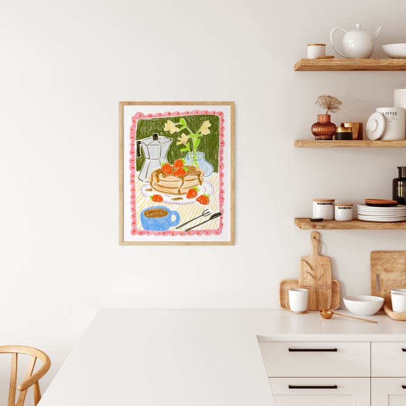 K&ouml;nnte beinhalten: Ein gerahmter Kunstdruck, der eine Fr&uuml;hst&uuml;cksszene zeigt. Die farbenfrohe Illustration zeigt Pfannkuchen mit Erdbeeren, eine Kaffeekanne, eine blaue Tasse und eine Vase mit Blumen. Das Kunstwerk ist vor einem gr&uuml;nen Hintergrund mit einem rosa Rand.