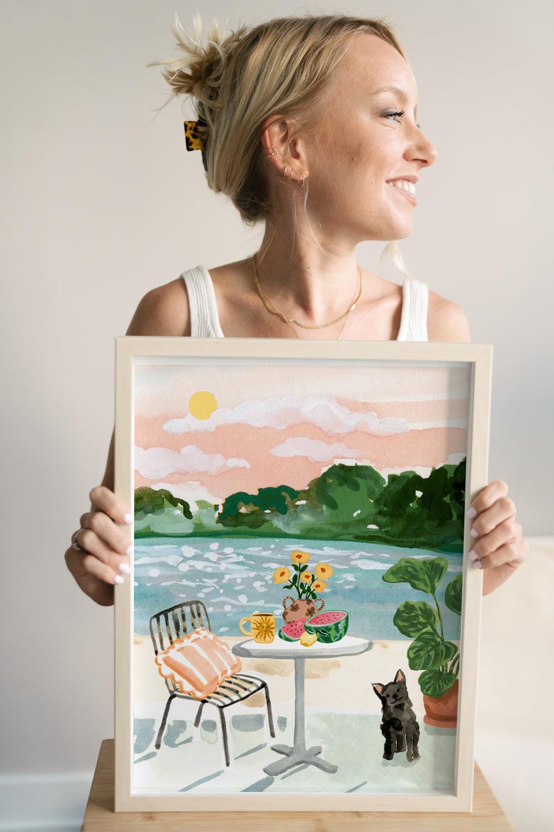 Puede incluir: Una pintura al agua enmarcada que representa una escena de un lago con una mesa y una silla, un jarr&oacute;n de flores amarillas, una sand&iacute;a, limones y un perro negro. El cielo es rosa y naranja con un sol amarillo.