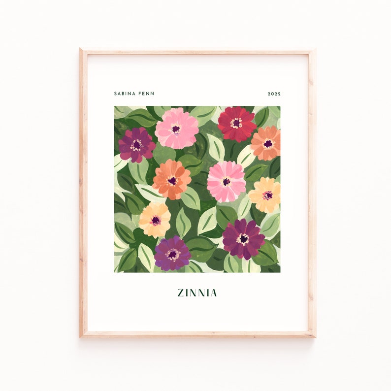 Puede incluir: Una impresi&oacute;n art&iacute;stica enmarcada con un dise&ntilde;o floral. La obra de arte presenta zinnias coloridas en tonos de rosa, rojo, naranja y morado, sobre un fondo de hojas verdes. El nombre de la artista, Sabina Fenn, y el a&ntilde;o 2022 est&aacute;n impresos en la parte superior, con la palabra "Zinnia" en la parte inferior.