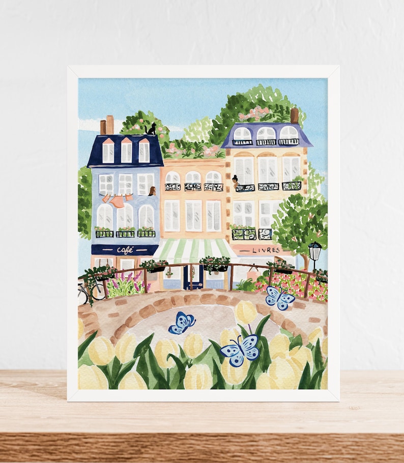 Op de afbeelding: Een aquarel schilderij van een Parijse straat sc&egrave;ne met kleurrijke gebouwen, een caf&eacute;, een boekwinkel en een brug met gele tulpen en blauwe vlinders. De tekst op het bord van het caf&eacute; luidt "caf&eacute;" en de tekst op het bord van de boekwinkel luidt "livres".
