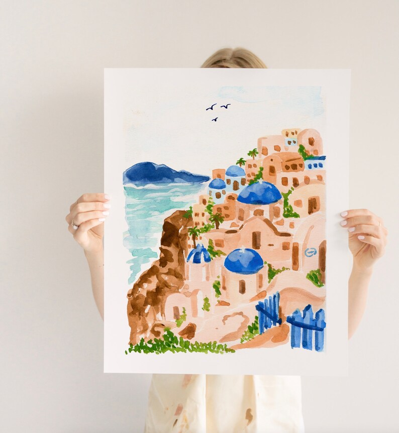Puede incluir: Pintura acuarela de un pueblo griego blanco y azul con edificios de c&uacute;pula azul en un acantilado con vistas al mar. La pintura tiene un cielo azul claro con algunas aves blancas volando.