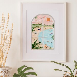 May include: A framed illustration of a beach scene viewed through a window. The window is divided into four panes and shows a beach with people swimming and sunbathing, palm trees, and a pink sunset.
