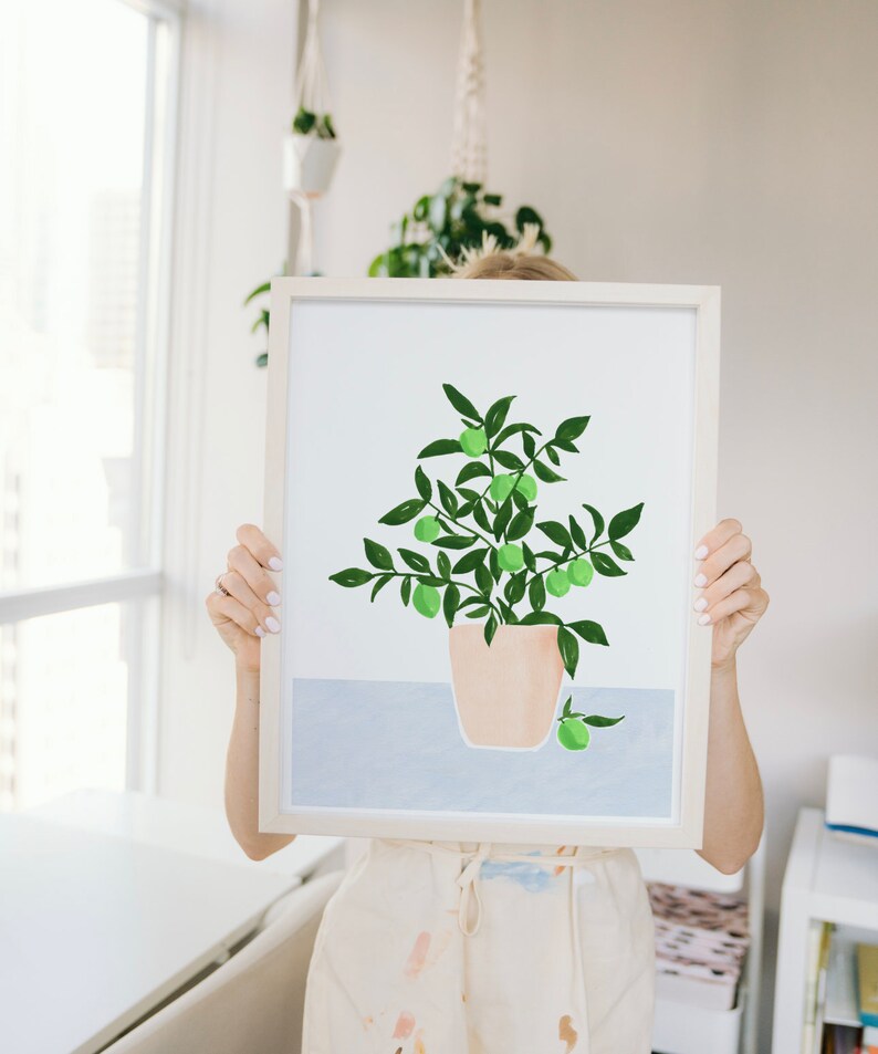 May include: A framed illustration of a potted plant with green leaves and small green fruit. The plant is in a light brown pot and is set against a light blue background.