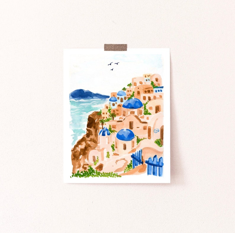 Puede incluir: Una pintura de acuarela de un pueblo blanco y azul en un acantilado con vistas al mar. Los edificios tienen techos abovedados azules y est&aacute;n rodeados de plantas verdes. Hay p&aacute;jaros volando en el cielo.