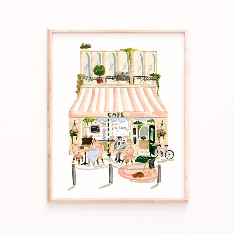 Op de afbeelding: Een aquarel schilderij van een Parijse cafe met een roze en wit gestreept luifel. De cafe heeft een bord met de tekst "Cafe Patisserie". Er zitten twee mensen aan tafels buiten de cafe, en er staat een fiets voor de cafe.
