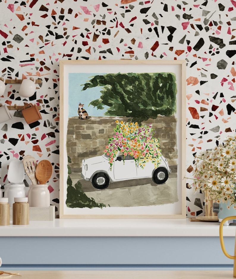 K&ouml;nnte beinhalten: Ein Aquarellbild eines wei&szlig;en Autos mit einem gro&szlig;en Strau&szlig; aus rosa, gelben und orangefarbenen Blumen darauf. Das Auto steht vor einer Steinmauer, auf der eine Katze sitzt.