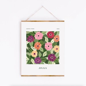 Puede incluir: Una impresi&oacute;n art&iacute;stica enmarcada con un dise&ntilde;o floral colorido. La obra presenta zinnias en tonos rosa, naranja, morado y rojo, sobre un fondo de hojas verdes. La impresi&oacute;n incluye el texto "Zinnia" y el nombre del artista.