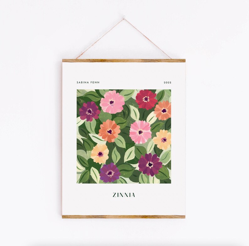 Puede incluir: Una impresi&oacute;n art&iacute;stica enmarcada con un dise&ntilde;o floral colorido. La obra presenta zinnias en tonos rosa, naranja, morado y rojo, sobre un fondo de hojas verdes. La impresi&oacute;n incluye el texto "Zinnia" y el nombre del artista.