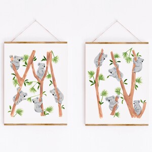 May include: Two framed prints with watercolor illustrations of koalas climbing on eucalyptus trees. The koalas are gray and the trees are brown with green leaves.