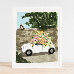 K&ouml;nnte beinhalten: Ein wei&szlig;es Auto mit einem gro&szlig;en Strau&szlig; bunter Blumen auf dem Dach, geparkt vor einer Steinmauer. Eine Katze sitzt auf der Mauer und schaut auf das Auto.