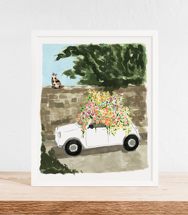 K&ouml;nnte beinhalten: Ein wei&szlig;es Auto mit einem gro&szlig;en Strau&szlig; bunter Blumen auf dem Dach, geparkt vor einer Steinmauer. Eine Katze sitzt auf der Mauer und schaut auf das Auto.