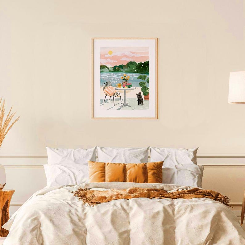 Puede incluir: Una pintura de acuarela de una escena de lago con una mesa y una silla instaladas en la orilla. Un gato negro se sienta en el suelo cerca de la mesa. La pintura tiene un cielo de puesta de sol rosa y naranja.