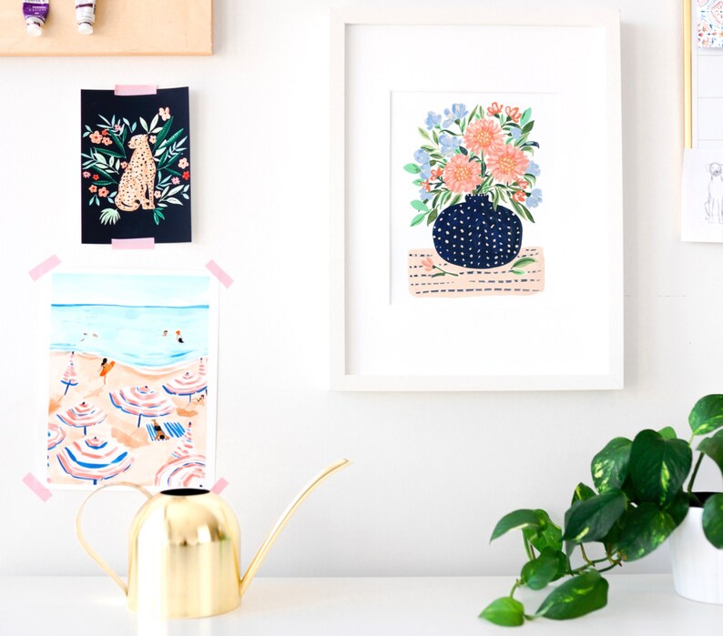 Puede incluir: Una ilustraci&oacute;n enmarcada de un ramo de flores rosas y azules en un jarr&oacute;n azul y blanco con lunares. El jarr&oacute;n est&aacute; sobre una alfombra de rayas rosas y blancas. La ilustraci&oacute;n est&aacute; enmarcada en blanco.