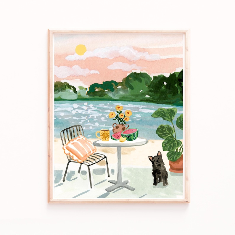 Puede incluir: Una pintura de acuarela de un conjunto de mesa y silla en una playa con un perro sentado cerca. La mesa tiene un jarr&oacute;n de flores amarillas, una taza y rodajas de sand&iacute;a. El fondo muestra un lago y &aacute;rboles con un cielo de puesta de sol rosa.