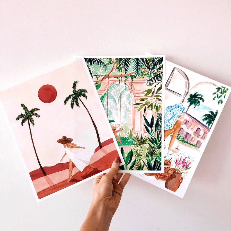 May include: Three watercolor prints featuring tropical scenes. The first print shows a woman in a white dress walking on a beach with palm trees and a red sun. The second print shows a lush green jungle with a stone archway. The third print shows a tropical house with palm trees and a blue sky.
