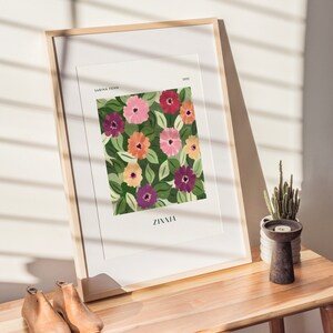 Puede incluir: Un cuadro enmarcado con un estampado floral de zinnias en tonos rosa, naranja y morado, con hojas verdes. La impresi&oacute;n se titula "Zinnia" y est&aacute; firmada "Sabina Fenn 2022".