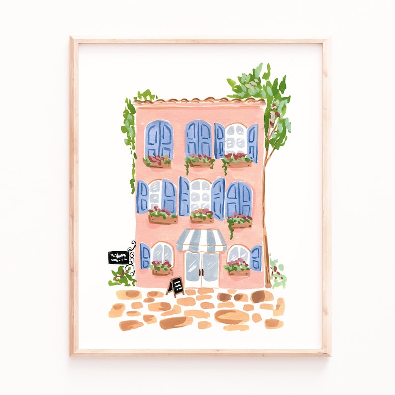 May include: A watercolor painting of a pink building with blue shutters and a striped awning. The building has flowers in pots on the windowsills and a sign that says "Bienvenue". The building is on a cobblestone street.