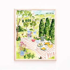 May include: A watercolor painting of a picnic scene in a green garden. A red and white striped tablecloth is laid out on the grass with a watermelon, fruit, and flowers. Two blue chairs are in the background with a green hedge and trees.
