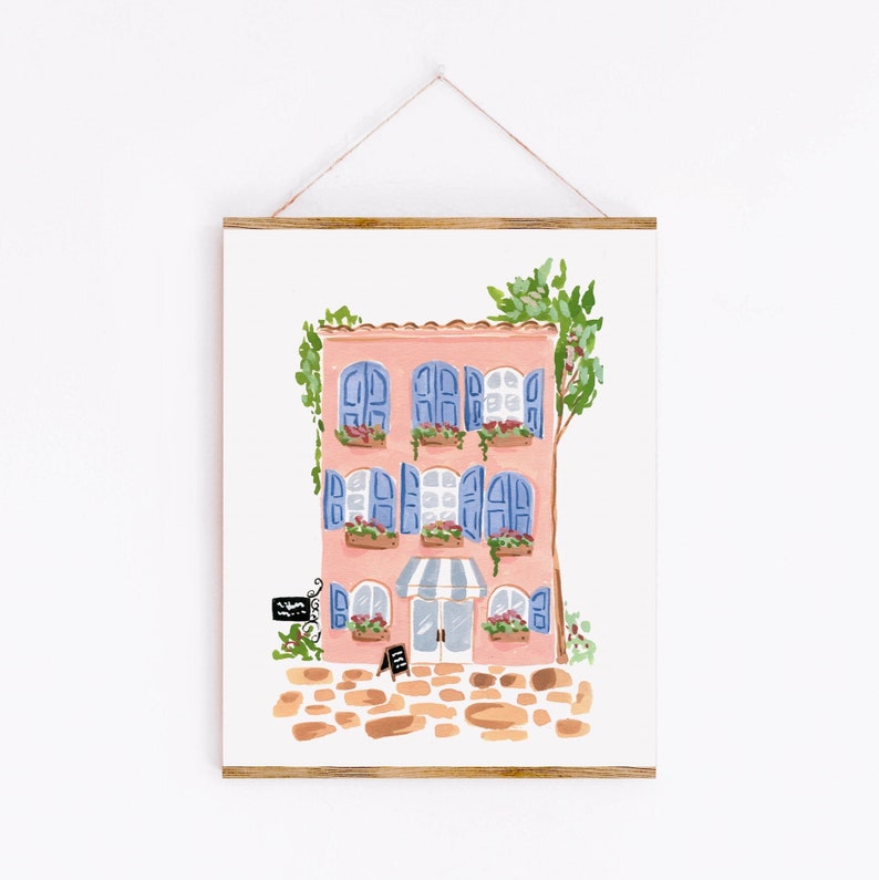 May include: A pink building with blue shutters and a striped awning. The building has flowers in pots on the windowsills and a sign that says "Salon". The building is surrounded by a cobblestone path.