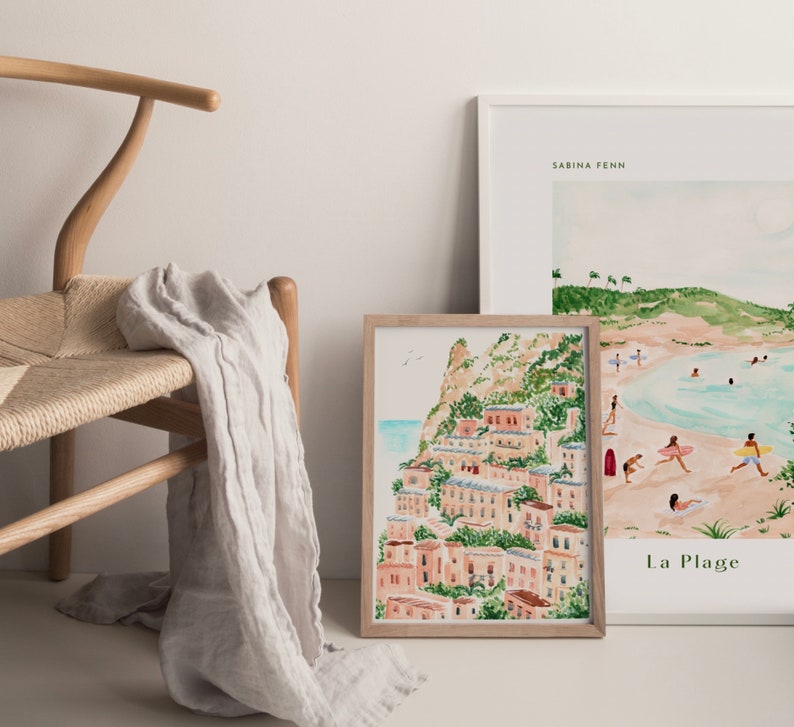 May include: Two framed watercolor paintings, one depicting a coastal scene with palm trees and the text "La Plage", the other depicting a hillside village with buildings and greenery.