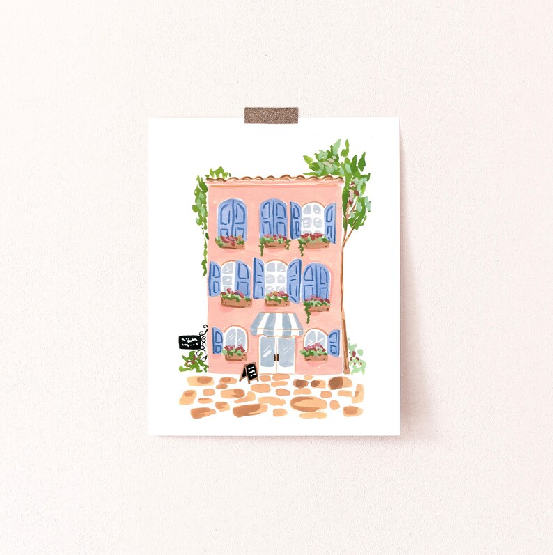 May include: A pink building with blue shutters and a striped awning. The building has flowers in pots on the windowsills and a sign that says "Bakery".